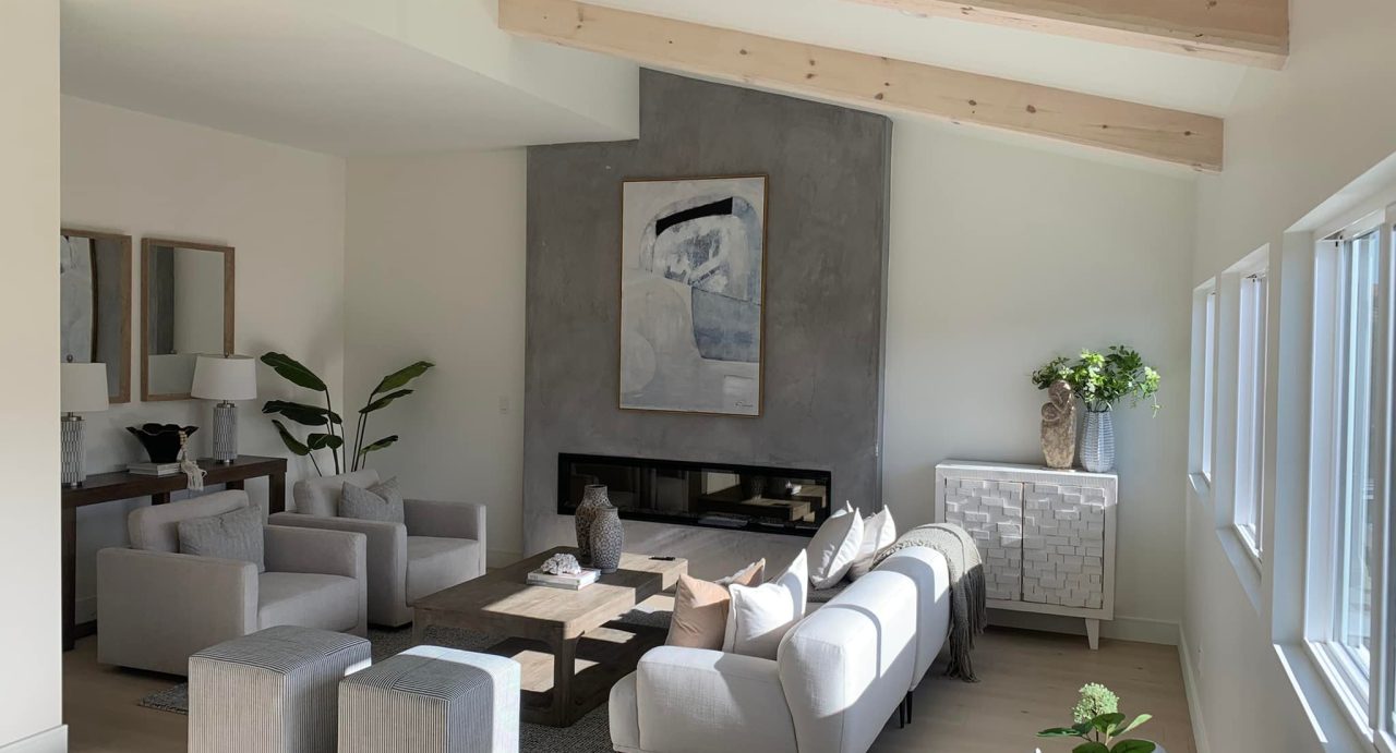 living room with white walls, foe finish fireplace accent wall, white ceiling with wood beams and grey couches.