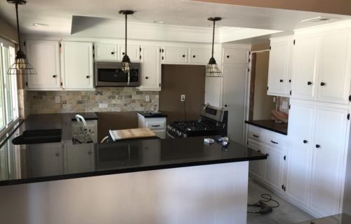 kitchen with white cabinets and black hardware, black quartz counterop and stone backsplash.