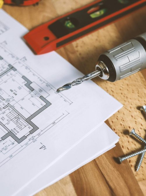 new construction blue prints sitting on a table next to level, pencil, drill, and screws.